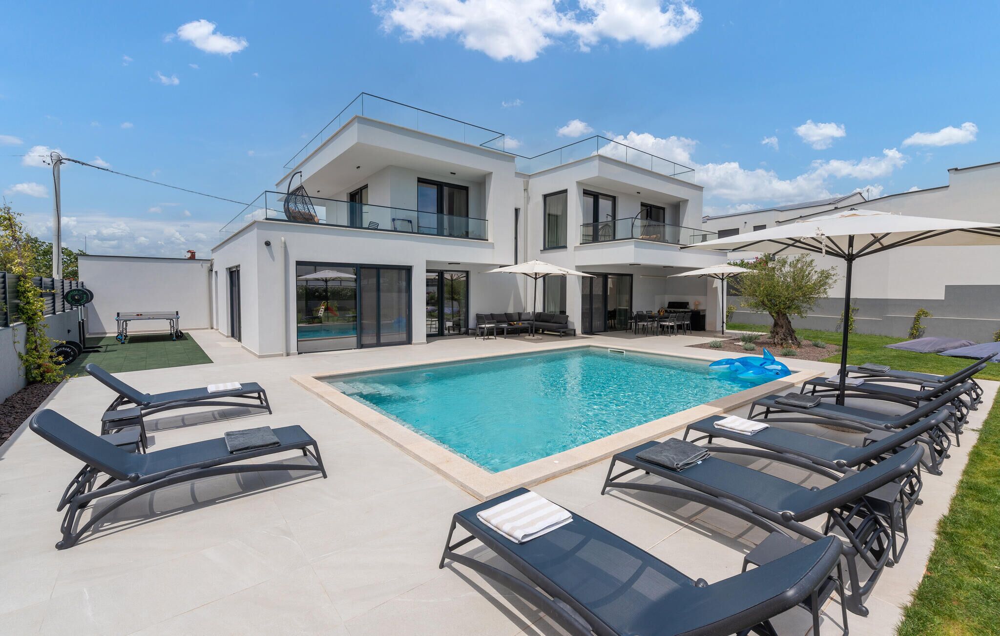 A modern two-story house with a swimming pool, outdoor seating, and a gym area.