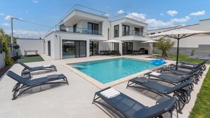 A modern two-story house with a swimming pool, outdoor seating, and a gym area.