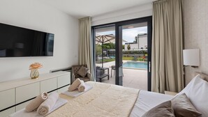 A hotel room with a bed, a TV, a desk, a chair, and a view of an outdoor swimming pool.