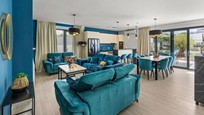 A modern living room with teal sofas, a dining area, and a kitchen.