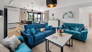 A modern living room with two blue sofas, a white coffee table, and a dining area with a table and chairs.