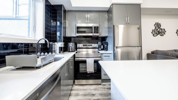A modern kitchen with stainless steel appliances, a large window, and a minimalist design. - Cozy 1BR with Parking, Only 7 Mins to The Falls and Sleeps 3! (Niagara Falls)