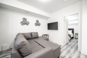 Un salon moderne avec un canapé d’angle, un téléviseur à écran plat et des œuvres d’art décoratives accrochées au mur.