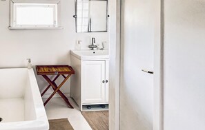 A bathroom with a white bathtub, a wooden stool, a white sink with a mirror above it, and a white door. - 2 bedroom gorgeous home in Hallaryd (Hallaryd)