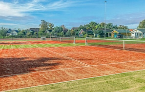A tennis court with a net, surrounded by green grass and trees. - Stunning (sta)caravan in Tzummarum (Tzummarum)