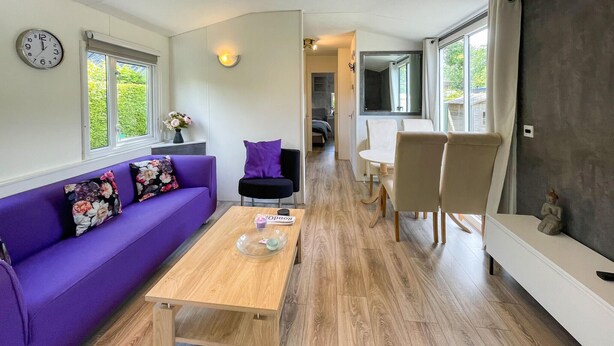 A modern living room with a purple sofa, a wooden coffee table, and a dining area with a white table and chairs. - Stunning (sta)caravan in Tzummarum (Tzummarum)
