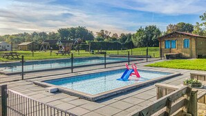 A rectangular pool with a slide, surrounded by a fence, and a small building with blue windows. - Stunning (sta)caravan in Tzummarum (Tzummarum)