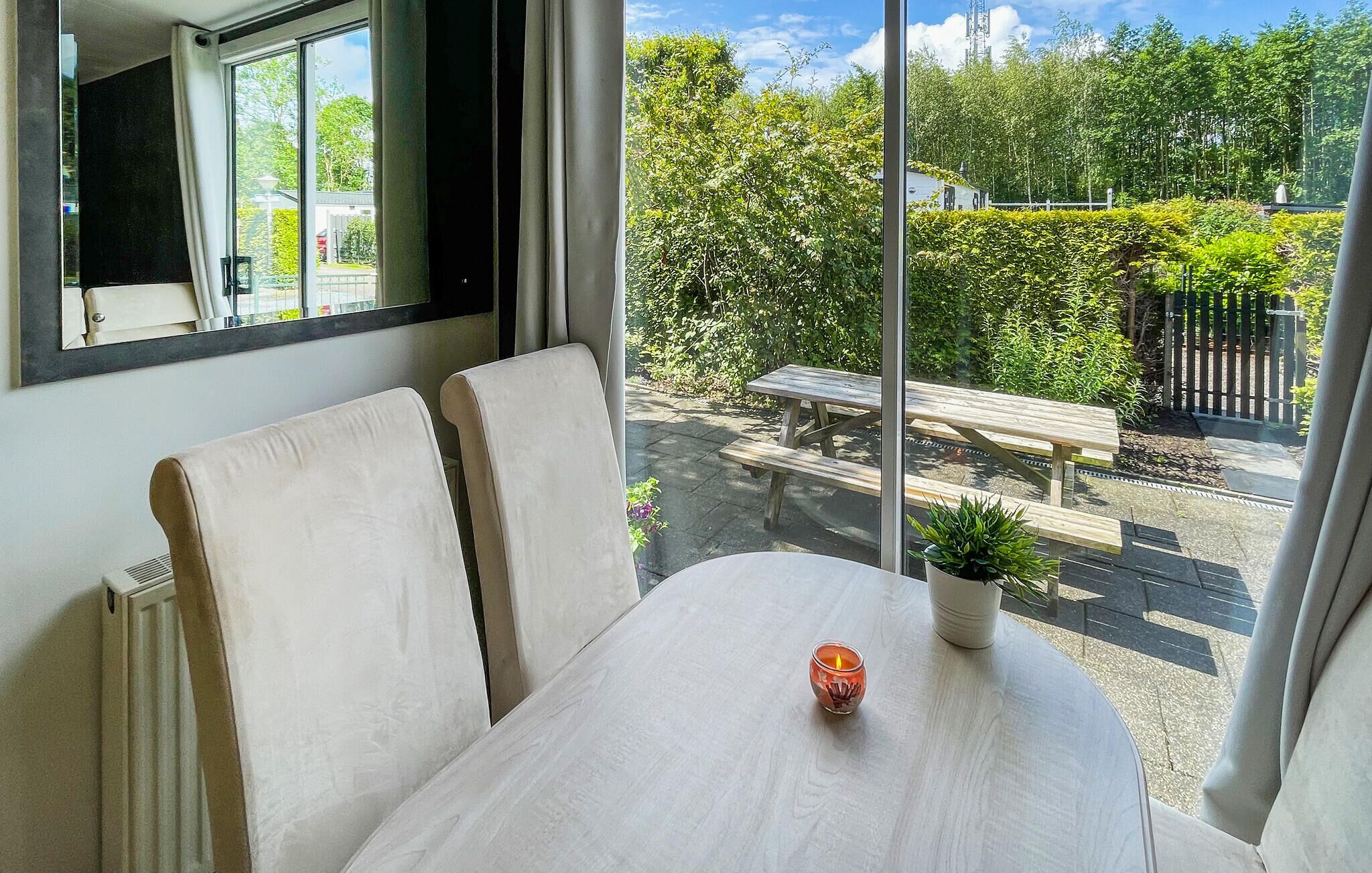 A room with a large window, a table with a potted plant, and a view of a garden with a bench and a fence.