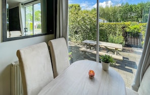 A room with a large window, a table with a potted plant, and a view of a garden with a bench and a fence. - Stunning (sta)caravan in Tzummarum (Tzummarum)
