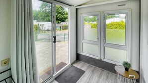 A room with a sliding glass door leading to an outdoor area, a small table with a plant, and a grey herringbone rug. - Stunning (sta)caravan in Tzummarum (Tzummarum)