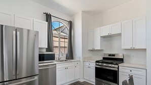 Una cocina moderna con electrodomésticos de acero inoxidable, armarios blancos y una ventana con cortinas.