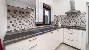 Una cucina moderna con zanzariera a scacchi, una finestra con tende e una cappa in acciaio inossidabile, oltre a mobili bianchi.