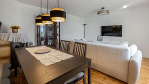 A modern living room with a wooden dining table, a sofa, and a TV mounted on the wall. - 2 bedroom lovely home in Grizane (Grizane)