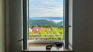 A room with a large window, a camera on the sill, and a view of a green landscape with buildings. - 2 bedroom lovely home in Grizane (Grizane)