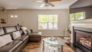 Un salon avec un canapé en cuir, une table basse en verre, une cheminée et un ventilateur de plafond.