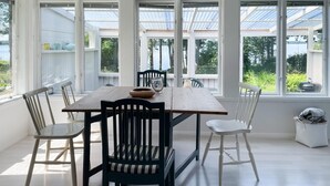 Ein Essbereich mit Holztisch und Stühlen, großen Fenstern mit Blick auf Grünflächen und einem hellen Interieur.