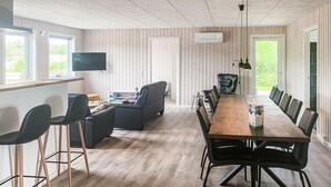 Ein moderner Essbereich mit einem langen Holztisch, schwarzen Stühlen und einem Fernseher an der Wand.