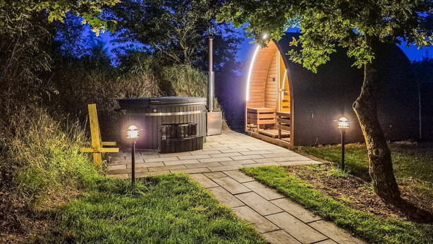 Eine Holzhütte mit gewölbtem Dach, vielleicht eine Sauna oder ein Whirlpool, umgeben von einem gepflasterten Weg und kleinen Lichtern.