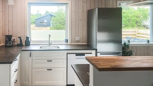 Eine moderne Küche mit Edelstahlkühlschrank, weißen Schränken, einer Holz Arbeitsplatte und einem Fenster mit Blick auf ein Haus und Grünflächen.