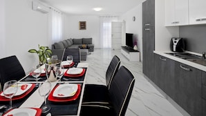 A modern dining area with a marble floor, a dining table set with red and white plates, and black chairs. There is a kitchen area with grey cabinets and a coffee machine. - Beautiful apartment in Umag (Umag)