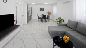 A modern living room with a flat-screen TV, grey sofa, and a dining area with a table and chairs. - Beautiful apartment in Umag (Umag)