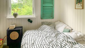 Een slaapkamer met een bed, een raam met luiken, een tafeltje met een doos en een wandlamp.