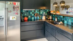 Een moderne keuken met donkere kastjes, een roestvrijstalen koelkast en een turquoise spatwand.