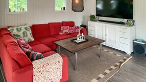 Een gezellige woonkamer met een rode hoekbank, een houten salontafel, een televisie en een witte kast.