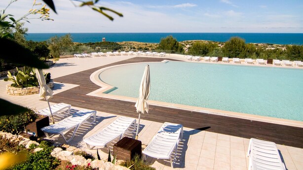 A poolside area with lounge chairs and a pool, surrounded by greenery and a view of the sea. - 1 bedroom awesome home in Vieste (Vieste)