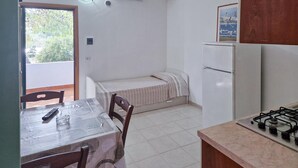 A compact kitchen with a dining table, chairs, a small bed, a refrigerator, and a gas stove. - 1 bedroom awesome home in Vieste (Vieste)