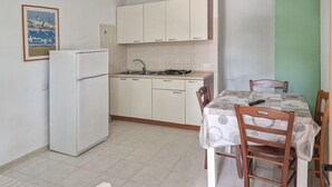 A compact kitchen with a refrigerator, sink, and stove, and a dining area with a table and chairs. - 1 bedroom awesome home in Vieste (Vieste)