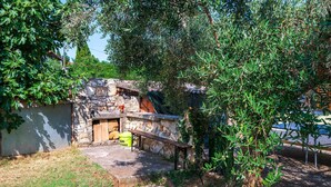 A stone-built outdoor kitchen area with a stone bench, a yellow bucket, and a wooden table. - Stunning home in Medulin with WiFi (Medulin)