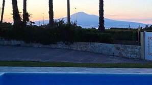 Une piscine avec un mur en pierre et une vue sur une montagne au coucher du soleil.