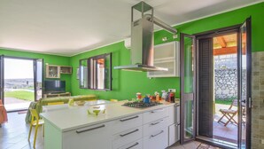 Une cuisine moderne dotée d’un grand îlot central, d’un four encastré et d’une cuisinière à gaz. On y trouve un coin repas avec une table et des chaises, ainsi qu’un téléviseur dans un coin.