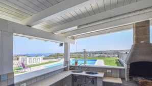 Une cuisine extérieure abritée, avec vue sur une piscine et l’océan.