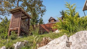 A wooden structure with a slatted roof, surrounded by greenery and rocks. - Beautiful home in Dobrenici with sauna (Dobrenici)