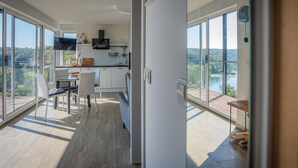 A modern kitchen with large windows, a dining area with chairs, and a view of a river and forest. - Beautiful home in Dobrenici with sauna (Dobrenici)
