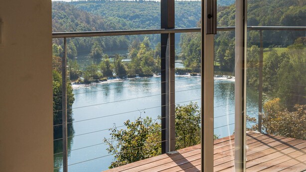 A view from a room with large windows overlooking a river with waterfalls, surrounded by forested hills. - Beautiful home in Dobrenici with sauna (Dobrenici)