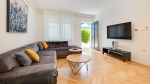 Un salon moderne avec un canapé gris, une table basse ronde en bois et un téléviseur à écran plat fixé au mur.