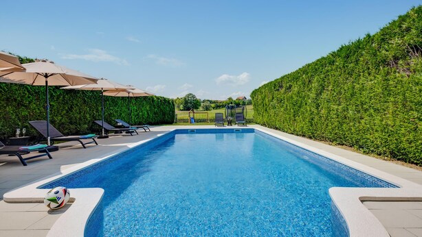Une piscine entourée de haies soigneusement taillées, avec des chaises longues et des parasols.