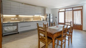 Cozinha moderna com ilha central, eletrodomésticos embutidos e área de refeições com mesa e cadeiras de madeira.