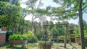 Um jardim com balanço de madeira, um muro de tijolos e diversas plantas.