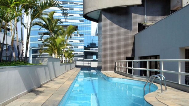 A swimming pool with a tiled deck, surrounded by palm trees and modern buildings in the background.