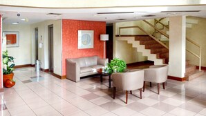 A lobby with a sofa, two armchairs, a coffee table, a staircase, and a potted plant.