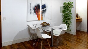A dining area with a glass table, white chairs, and a plant.