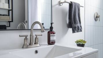 A bathroom with a white sink, a silver faucet, a bottle of hand soap, a towel rack with a towel, and a small potted plant.
