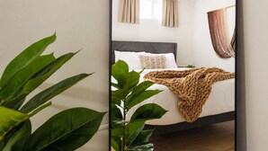 A modern hotel room with a bed, a large window with curtains, a plant, and a hanging curtain.