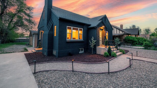 A modern house with a dark exterior, a chimney, and a well-maintained front yard with gravel and a pathway.