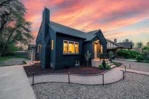 Une maison moderne à l’extérieur sombre, dotée d’une cheminée et d’un jardin bien entretenu avec du gravier et un chemin.