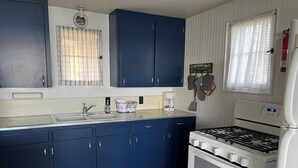 Une cuisine avec des meubles de couleur bleue, une cuisinière blanche et une fenêtre avec des rideaux.